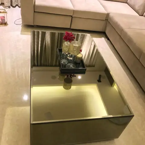 Mirror-clad rectangular coffee table with a backlit inner well and a black bar tray, shot from above against an L-shaped beige suede sectional on cream marble