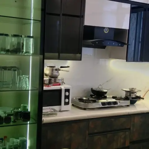 Modular kitchen with dark textured laminate shutters, glossy white overhead cabinets, chimney hood over a gas cooktop, and a green-lit glass crockery unit