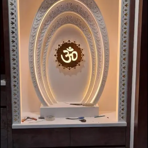 Multi-layered arched pooja unit backlit with warm cove lighting and a central carved Om medallion