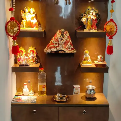 Multi-tier wall-mounted pooja unit with lit niches for deity idols, garlands, and drawer storage below.