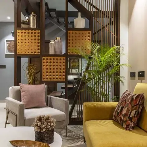 Mustard sofa and grey armchair around a white round table, screened from the staircase by a dark wood grid partition with cane-webbed square inserts