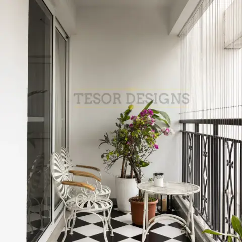 Narrow apartment balcony floored in a black-and-white diamond checkerboard, with two white wrought-iron sunburst-back chairs with teak arm caps