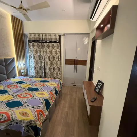 Narrow bedroom shot lengthwise: patchwork-print bedspread on a bed with a grey tufted headboard, a backlit fluted panel strip beside it