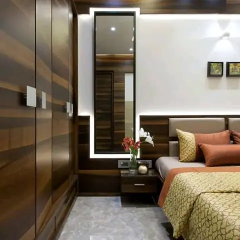 Narrow bedroom with a floor-to-ceiling walnut wardrobe run down one side, a tall mirror set inside a bright continuous LED frame on the wood-panelled end wall