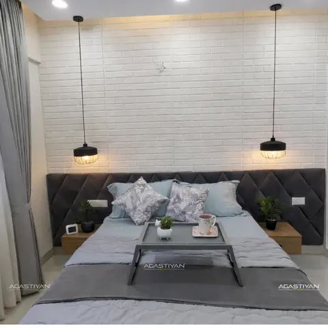 Narrow bedroom with a white-painted brick-clad headboard wall, twin caged black pendants dropping either side of a grey diamond-tufted headboard