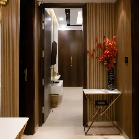 Narrow entrance foyer lined on both sides with slim fluted wood panelling, a gold X-frame marble console holding a red faux-blossom vase