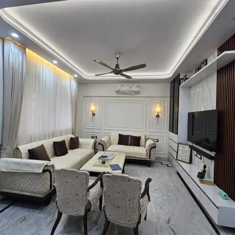 Narrow Indian living room with white PU moulding panels and two brass sconces behind a cream tufted sofa