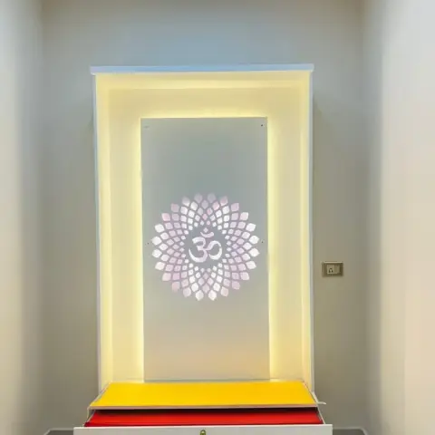 Narrow pooja alcove with an Om-in-lotus mandala cut into a translucent back panel, glowing from a recessed white frame