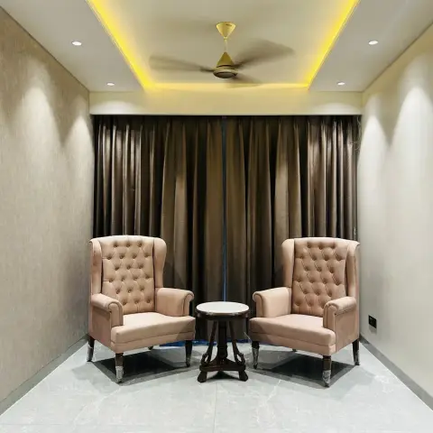 Narrow seating nook with two blush button-tufted wingbacks facing each other across a small marble-top round table, against bronze floor-length curtains.