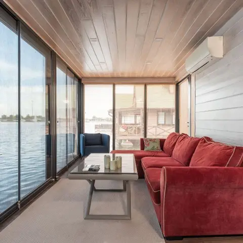 Narrow waterside living room with a red sectional sofa, a navy accent armchair and floor-to-ceiling glass looking out over the lake.