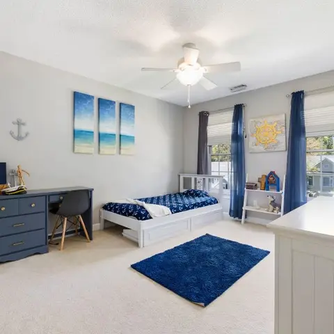 Nautical-themed boy's bedroom with a navy anchor-print trundle bed, ocean-triptych wall art, a grey desk and blue shag rug