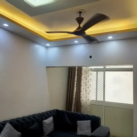 Navy chesterfield-style tufted sofa with houndstooth cushions under a gold cove-lit ceiling with a crystal flush-mount fixture.