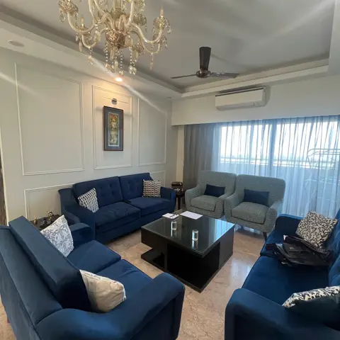 Navy velvet sofa seating arranged around a black coffee table beneath a crystal chandelier, with white panel-moulded walls.
