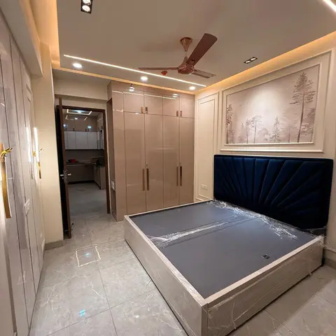 New-handover bedroom with a fan-pleated navy velvet headboard on a still plastic-wrapped storage bed, glossy champagne wardrobe