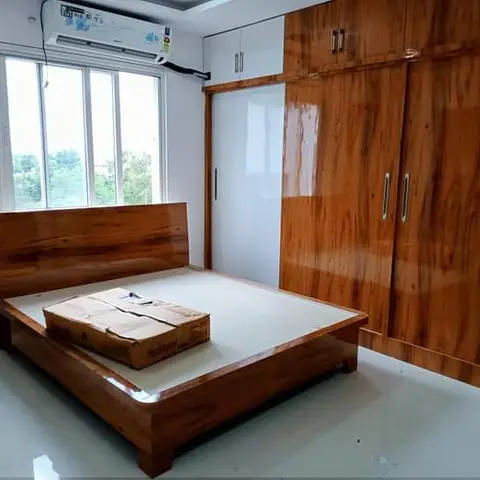 Newly finished bedroom with a glossy wood-grain laminate bed frame and matching sliding-door wardrobe, still unstyled with bare walls and a split AC.