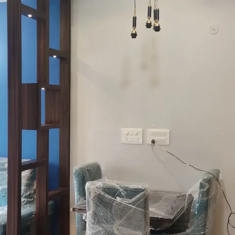 Newly finished dining nook with a wood-beam ceiling, brass-finished pendant lights and a blue accent wall, furniture still wrapped in protective plastic.