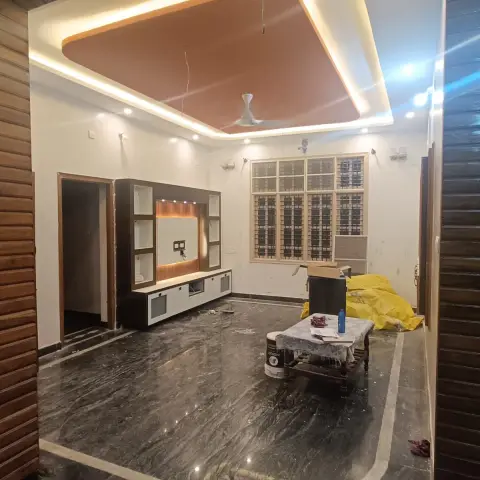 Newly finished living room seen through a wood-clad arched opening, with a terracotta POP ceiling drop on concealed cove light and a laminate TV unit above a