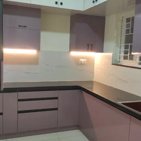 Newly fitted L-shaped kitchen in mauve high-gloss shutters with a black granite counter, a marble-look slab dado washed by under-cabinet strips
