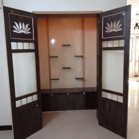 Newly fitted pooja mandir with lotus-cutout and frosted-glass folding shutters swung open to staggered display shelves over a closed storage base