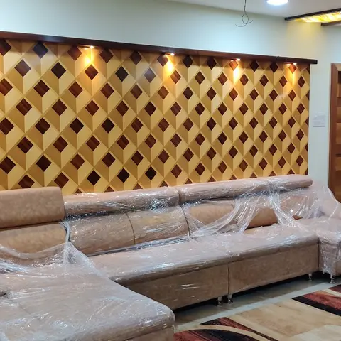 Newly furnished living room with a diamond-parquet wood feature wall lit by recessed spotlights, and a large L-shaped sofa still wrapped in factory plastic.