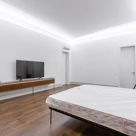 Newly handed-over bedroom with cove-lit ceiling, a floating walnut TV console, and a mattress still wrapped in factory plastic on a bare bed frame