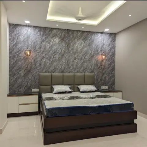 Newly handed-over bedroom with the mattress still in its factory plastic — grey marble-look slab wall behind a grid-stitched beige headboard