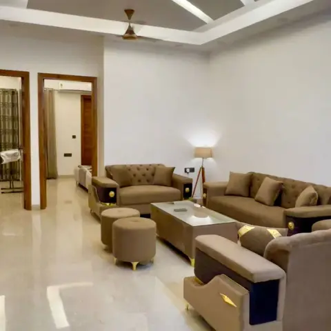 Newly handed-over drawing room with the shop tags still tied to a brown velvet sofa set, under an angular white-ribbed POP frame set into a grey ceiling recess.