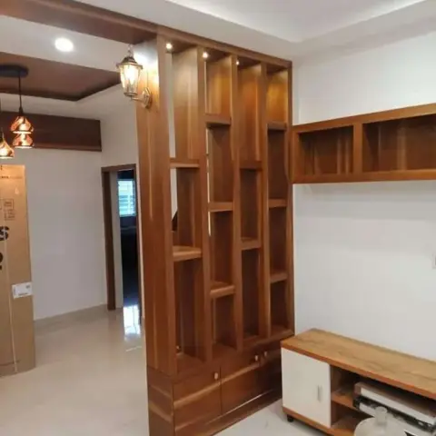 Newly handed-over hall where a floor-to-ceiling teak-toned open-grid display partition with lit niches and drawer bases screens the passage