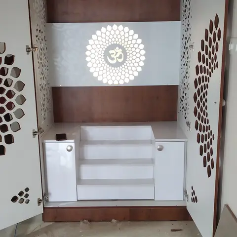Newly installed white pooja cabinet with jaali-cut cutwork doors and a backlit Om lotus panel, floor still dusty with tools from installation.