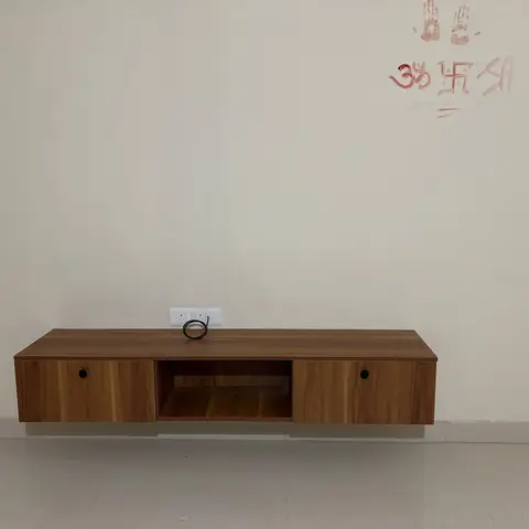 Newly installed wood-laminate floating TV console mounted on an otherwise bare wall marked with fresh griha pravesh handprints.