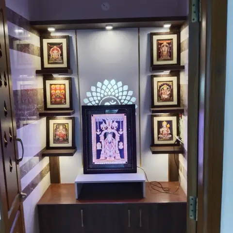 Niche pooja unit behind carved teak doors, with six framed deity pictures stepped on wenge floating shelves either side of a backlit acrylic Om-and-lotus motif