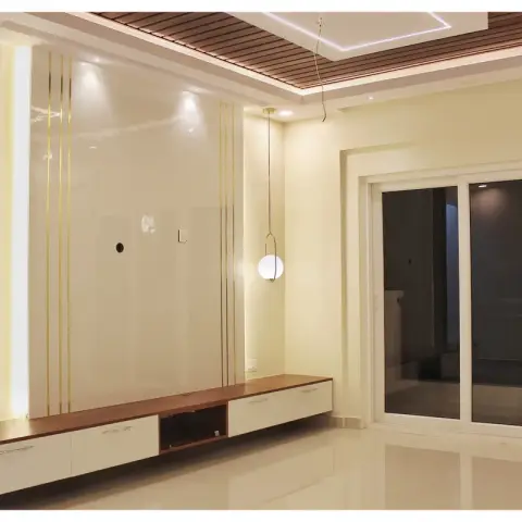 Night photo of a handed-over living room where the cream gloss TV panel is ruled with thin gold inlay lines beside a walnut-framed bronze mirror in a diamond