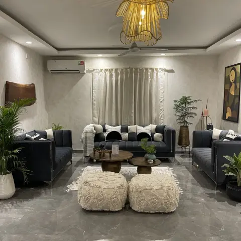 Night shot of a living room arranged symmetrically with three charcoal channel-tufted sofas around two round mango-wood tables