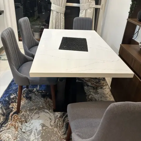 Night-time dining set-up with a white stone-top table on a black pedestal base, grey channel-stitched chairs