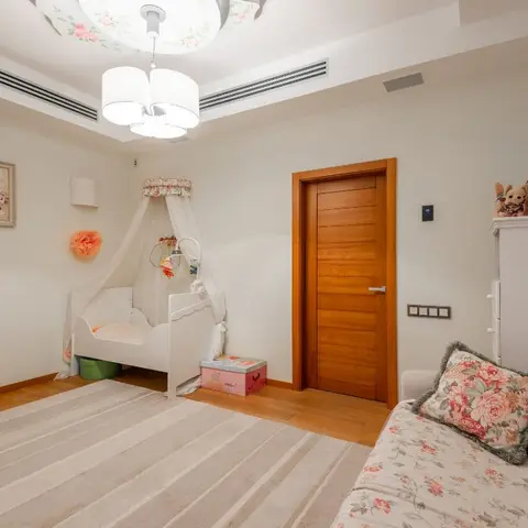 Nursery with a white canopy-draped crib, a rose-motif ceiling light fixture, floral wall art and stuffed toys stacked on a dresser beside a floral-upholstered