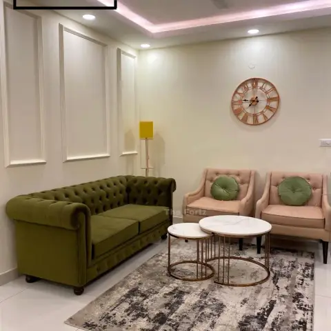 Olive velvet Chesterfield facing two blush tufted armchairs with round green bolsters