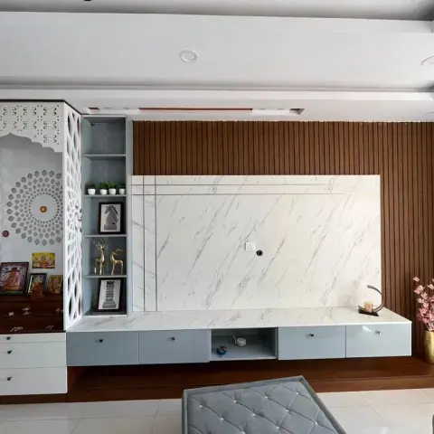 One continuous wall pairing a white CNC-jaali pooja unit with an Om cutout against a marble-panelled TV back and a fluted teak wall