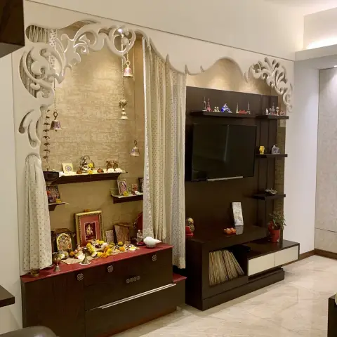 One living-room wall carries a curtained pooja niche with hanging brass bells and a red-topped wenge storage base on the left
