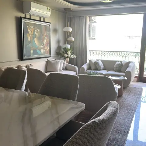 One long room running from a white onyx-look dining table with boucle chairs in front to a curved cream sofa set at the balcony end