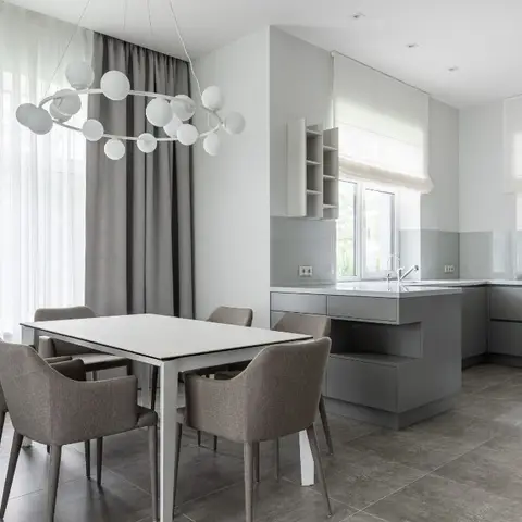 Open dining and kitchen space with a sculptural globe chandelier over a marble-top dining table, grey upholstered armchairs