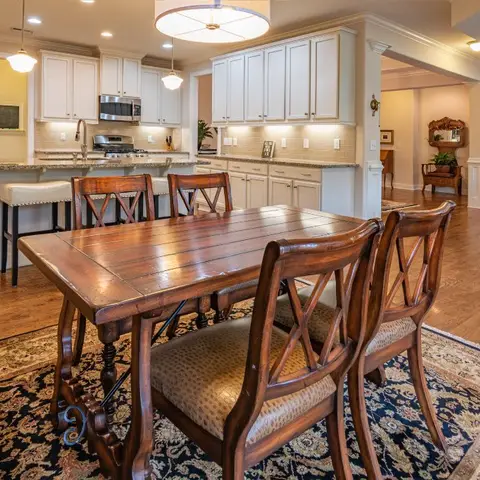 Open dining and kitchen with a wood farmhouse-style table on a patterned oriental rug, a white raised-panel kitchen island with barstool seating