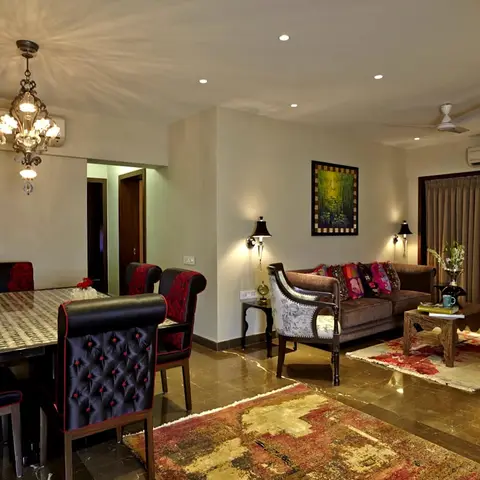 Open dining-and-living area with a black tufted dining set, brass chandelier, and a red-toned patchwork rug anchoring the seating zone.