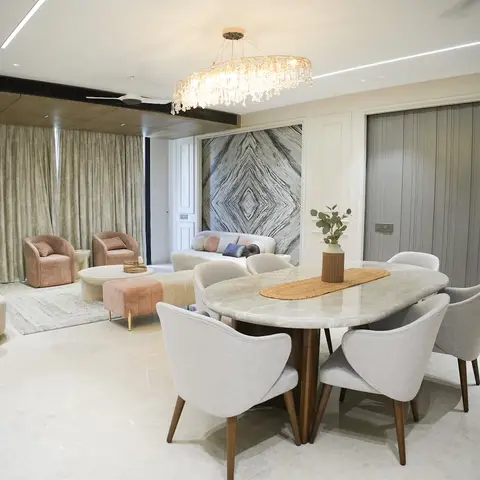 Open dining and living area with an oval marble dining table beneath a crystal ring chandelier, a book-matched marble accent panel