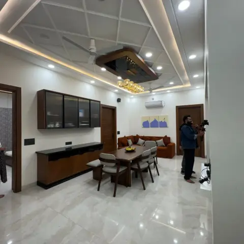 Open dining and living area with a triangular cove-lit POP false ceiling and mirrored pendant, a wall-mounted glass-shutter crockery unit