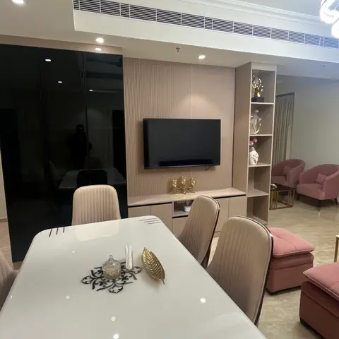 Open dining-and-living space with a glossy white dining table in the foreground, a fluted-panel TV wall with open display shelving