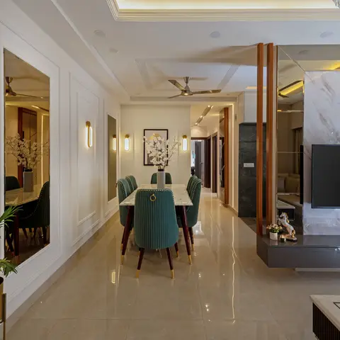 Open dining-and-living space with green velvet chairs around a marble table, a mirrored panel wall, and a marble-clad TV wall unit beyond.