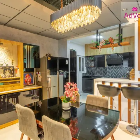 Open dining area with a black stone-top table and velvet chairs beneath an oversized crystal chandelier, a wood-framed pooja unit with a lit Om motif backdrop