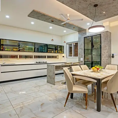 Open dining area with a marble-top table and cream velvet chairs under a drum pendant light, a glass-front crockery display and stone-clad breakfast counter