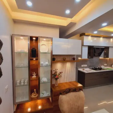 Open dining area with a wood-and-glass crockery display cabinet lit from within, a fluted panel accent wall, and a view through to the kitchen.