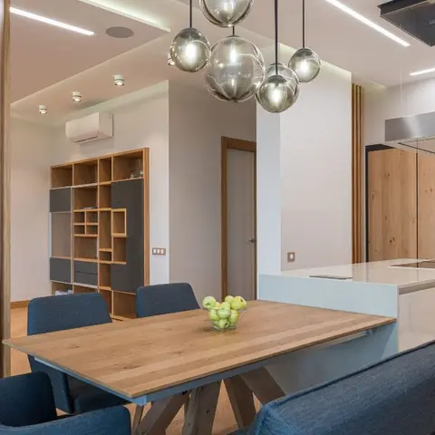 Open dining area with a wooden trestle table, navy upholstered chairs, a cluster of smoked-glass sphere pendant lights, and a fluted wood-slat partition